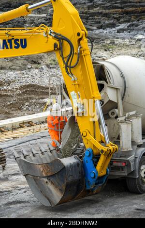 PORTHCAWL, WALES - JUNE 2018: Concrete mixer unloading ready mixed concrete into the bucket of a heavy duty excavator for sea defences Stock Photo