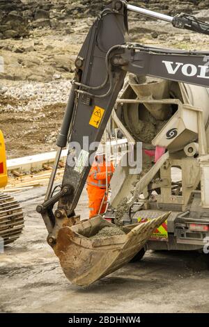 PORTHCAWL, WALES - JUNE 2018: Concrete mixer unloading ready mixed concrete into the bucket of a heavy duty excavator for sea defences Stock Photo