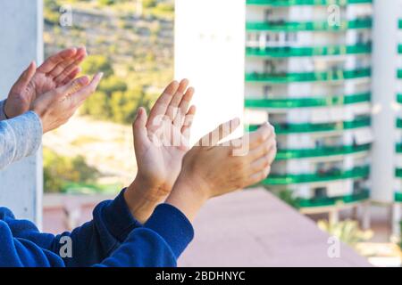 Family applauding medical staff from balcony. People clapping on balconies and windows in support of health workers during the Coronavirus pandemic Stock Photo