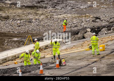 PORTHCAWL, WALES - JUNE 2018: Construction operatives working at low tide on the redevelopment of the seafront in front of the town's promenade Stock Photo