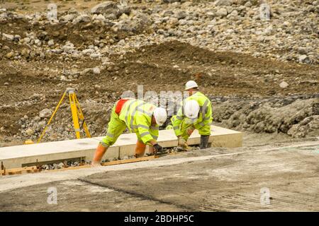 PORTHCAWL, WALES - JUNE 2018: Construction operatives laying concrete on rocks on the seafront in Porthcawl to improve its appearance Stock Photo