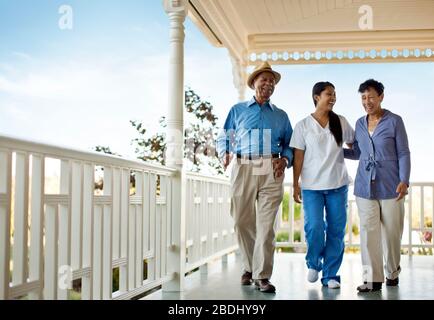Nurse walking with senior couple on deck of rest-home. Stock Photo