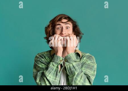 Curly teenager biting his nails in fear on color background Stock Photo