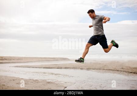 Young man jumping over shallow water on a beach. Stock Photo