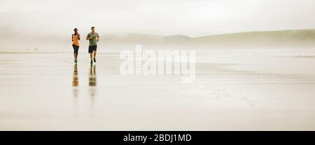 Young couple running together on a beach at low tide. Stock Photo