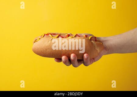 Hand holds tasty hot dog on yellow background Stock Photo