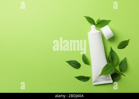 Toothpaste tube and mint leaves on green background, space for text Stock Photo