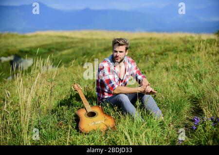 Guy with guitar contemplate nature. Inspiring nature. Pleasant time alone. Musician looking for inspiration. Dreamy wanderer. Wanderlust concept. Summer vacation highlands nature. Peaceful mood. Stock Photo