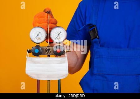 An air conditioning technician holds pressure gauges in his hand for refueling air conditioners. Medical face shield on measuring equipment for filling air conditioners. Stock Photo