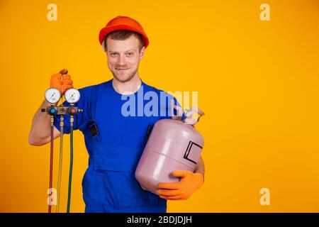 Young cheerful smiling air conditioning specialist. Repair of air conditioners and manometers, measuring equipment for refueling air conditioners. On a yellow background Stock Photo