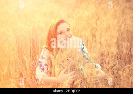 Beautiful young woman lying in field of  looking at you camera. Beauty Romantic Girl Outdoors. Teenage girl in white blue dress in sun light holding w Stock Photo