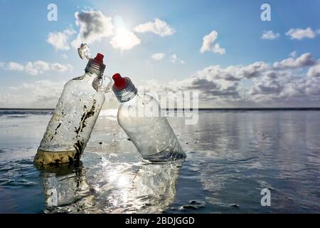 Plastic bottles with red bottle caps standing in the sea with blue sky and backlight at low tide. Concept of plastic pollution of the sea. Stock Photo