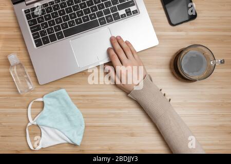A protective mask and bottle with dizenfector on a desk. Close up womans hand on a touchpad. Health care during pandemic of SARS-Cov-2. Stock Photo