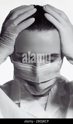 Black and white portrait of tired female doctor putting hands on head from pain Stock Photo