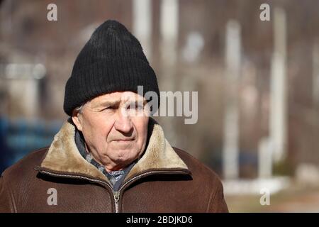 Elderly man standing on rural background in sunny spring day. Sad face expression, concept of walking during coronavirus quarantine, life in village Stock Photo