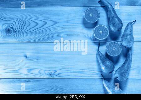 Juicy sliced orange tangerines and pears of the English Conference variety lie on a textured yellow wooden table. Tinting in Classic Blue. Space for t Stock Photo