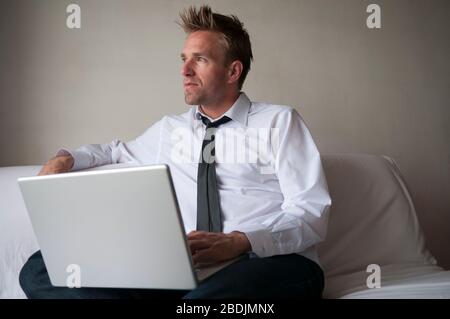 Man in stylish outfit sitting at home on the sofa browsing his laptop computer Stock Photo