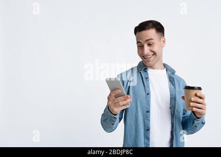 Guy is looking at smartphone, holding cup Stock Photo