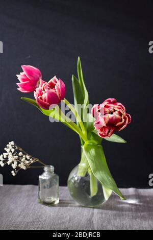 Three red terry tulips in a round vase with small pharmaceutical bottles on a black background