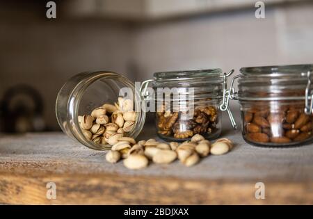 Pistachios scattered on the white vintage table from a jar and with other nuts on background. Pistachio is a healthy vegetarian protein nutritious Stock Photo