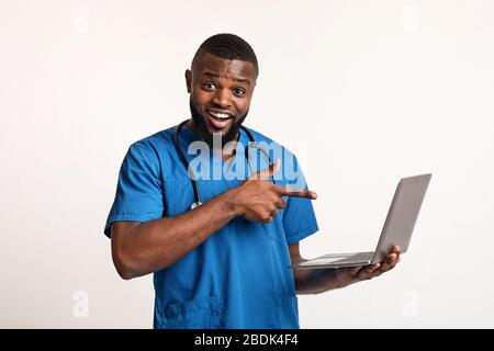 Emotional black doctor holding laptop over white background Stock Photo