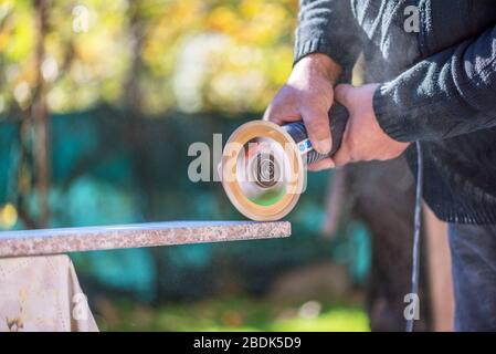 Grinder worker cuts stone block with electric hand saw. Stock Photo