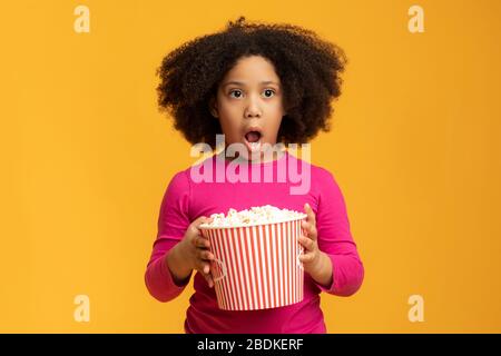 Shocked little african girl eating popcorn and opening mouth in amazement Stock Photo
