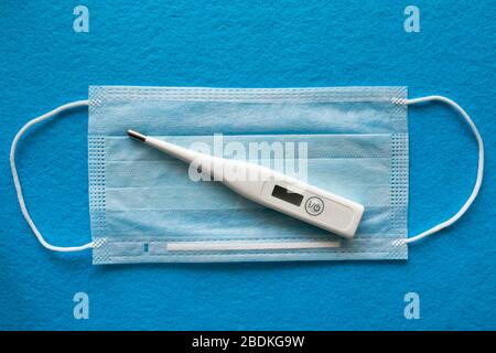 Medical mask for protection against coronavirus. Surgical protective mask and thermometer for measuring temperature lies on the medical mask. Medical respiratory bandage for face. Stock Photo