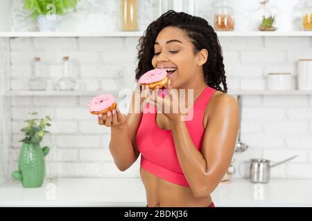 Happy Slim Black Girl Eating Two Doughnuts Stock Photo