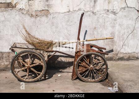 Suzhou China - May 3, 2010: Closeup of 2 brown rusted wheelbarrows set against white wall and broom made of twigs. Stock Photo