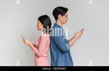 Asian girl and guy standing back to back, using cellphones Stock Photo