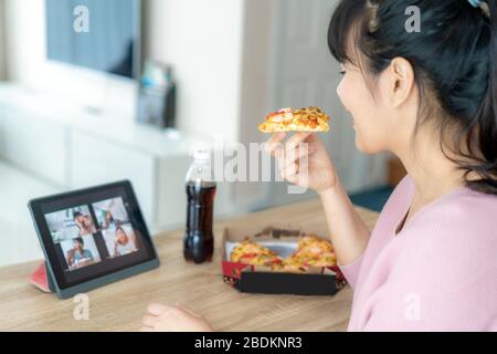 Asian woman virtual happy hour meeting party and eating food online together with her friend in video conference with digital tablet for a online meet Stock Photo