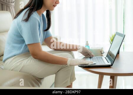 Asian woman is spraying alcohol, disinfectant spray on laptop computer, prevent infection of Covid-19 virus, wipe or cleaning phone to eliminate, outb Stock Photo