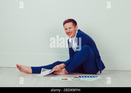 Smiling laughing Woman looking at her project work plans in her new house holding them up in her hands as she sits on the floor in an empty white room Stock Photo