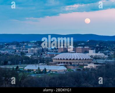 Morgantown, WV - 7 April 2020: Super pink moon rises above the coliseum arena on the Evansdale campus of WVU university Stock Photo