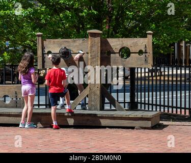 Two children, a boy, and a girl standing before a man in stocks in the courtyard of the Old State House, downtown Hartford CT Stock Photo