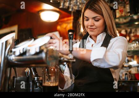 A young attractive blonde caucasian  waitress pouring beer in a cafe Stock Photo