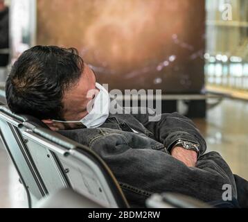 Man wearing a medical face mask while sleeping in a chair in an airport waiting area Stock Photo
