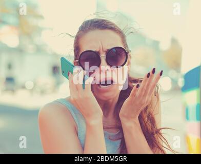 Portrait angry young woman screaming on mobile phone standing outside with city background. Negative emotions feelings Stock Photo