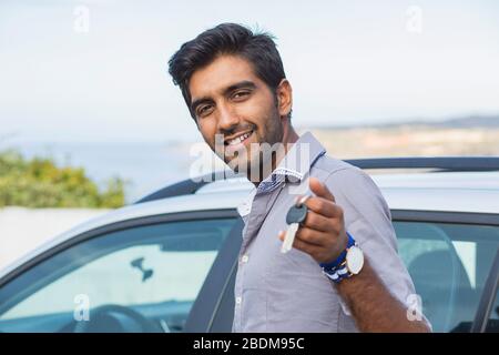 Closeup portrait happy, smiling, young man, buyer showing keys of his new car isolated outside dealership lot. Personal transportation, auto purchase Stock Photo