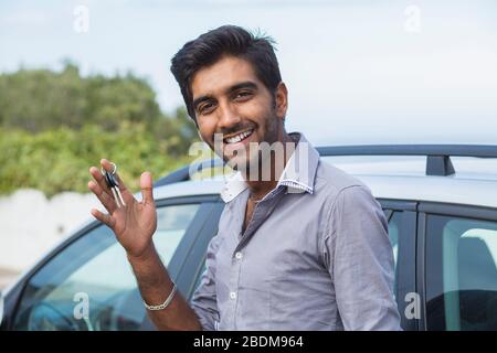 Closeup portrait happy, smiling, young man, buyer showing keys of his new car isolated outside dealership lot. Personal transportation, auto purchase Stock Photo