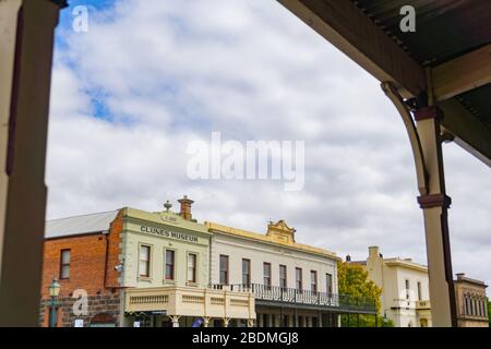 Clunes Australia - March 15 2020; Historic buildings Clunes Museum and Club Hotel  framed by veranda across road. Stock Photo