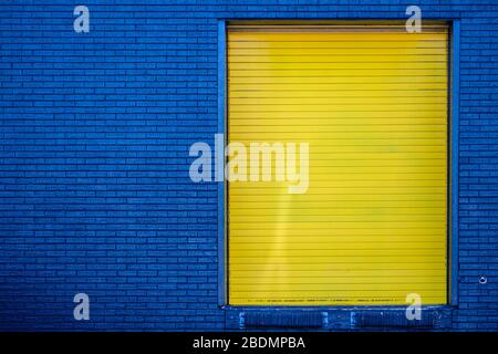 Dark blue brick wall and contrsting bright yellow loading-dock door. Stock Photo