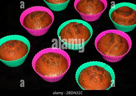 Nine freshly baked muffins in purple and green cups on a black background Stock Photo