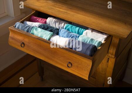 Woman's shirts in an antique wood bureau drawer folded in the KonMari method of home organization expert Marie Kondo. Stock Photo