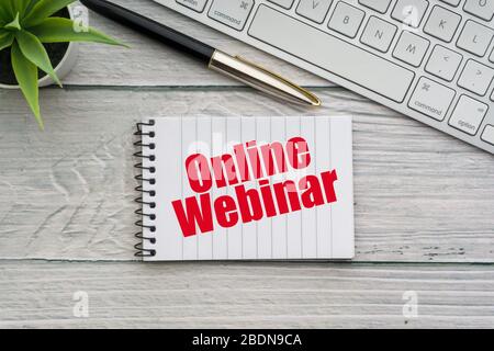 ONLINE WEBINAR text with decorative flower, fountain pen, keyboard and notepad on wooden background. Business and technology concept Stock Photo