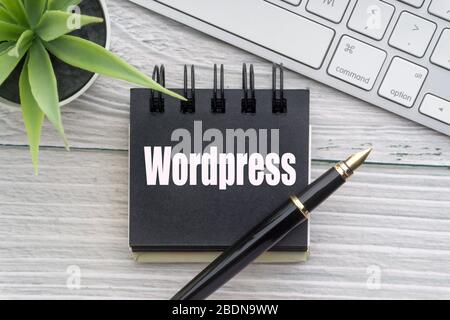 WORDPRESS text with decorative flower, keyboard, notepad and fountain pen on wooden background. Business and technology concept Stock Photo
