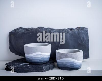 Cactus pot. Concrete pot. Two empty modern geometric concrete planters with painted on rock on white wooden shelf isolated on white wall background. Stock Photo