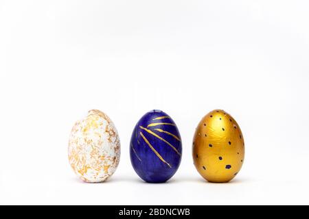 Three easter eggs trendy colored classic blue, white and golden decorated on white table. Happy Easter card with copy space for text. Minimal style Stock Photo