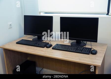 two computers and a desk . Keyboard and mouse . Two computer monitors with a black screen on a desk . Stock Photo